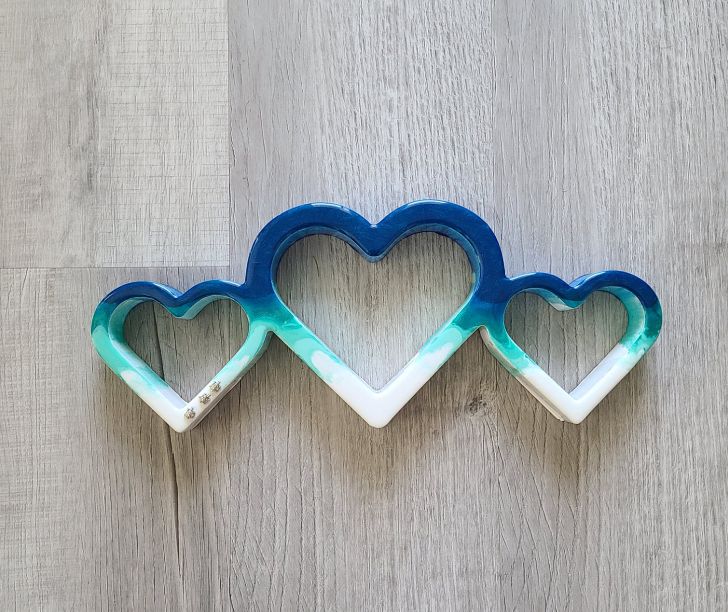 The three hearts connect to the ocean and features three little turtles racing toward the water. One of a kind piece. UV Resistant resin on wood Turtles are metal Stand or hang Approximate measurements: 14.5 x 6 x 1.25 inches