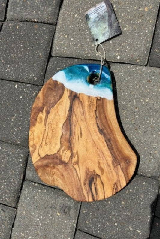 Nice Olive Wood Cutting Board has a corner of foamy ocean waves of resin. The live edge gives it a rustic feel. Nice 1 inch thick board. Deep turquoise, blue, green and white give this board lots of movement. Resin is Food Safe and UV Resistant Approximate size: 10.5 x 7.5 x 1 inches Weight: 1 pound, 13 ounces