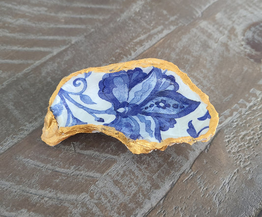 Beautiful, handcrafted oyster shell can be used alone or as a trinket holder. Blue flower on white background. Trimmed in gold paint. Coated with 2 coats of Varnish. The back has a coat also to protect it from flaking and leaving dust behind. Note: Rings NOT included Approximate size: 3.75 inches at the longest point, 2 inches wide at the widest point.