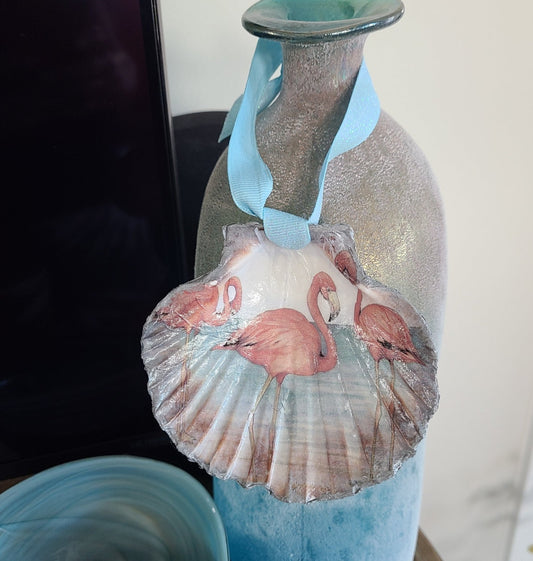 I decorated this clam shell with a design of three flamingos. The back side looks like wave ripples. The edges are trimmed in metallic silver. A blue iridescent ribbon is tied on for hanging. Acessories shown are NOT included. Approximate size: Shell: 4 x 4.25 inches
