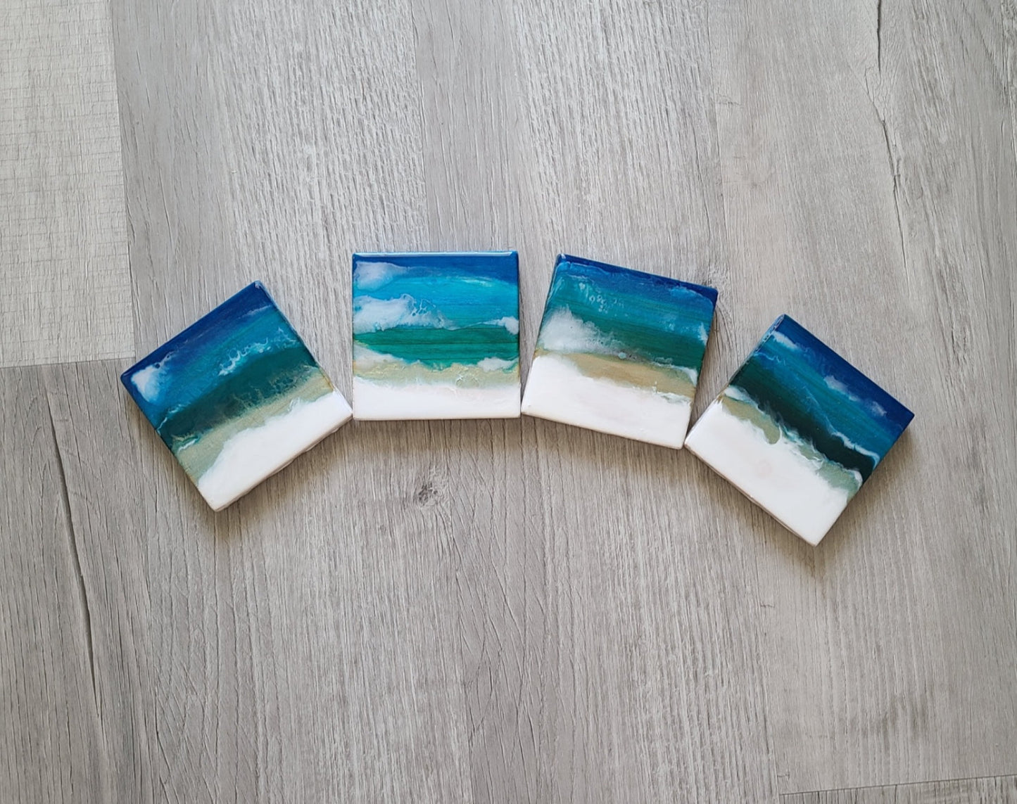 These fun coasters are lightweight. Each one is different. White water crashes over the sparkling blues and iridescent greens. Truly one-of-a-kind. Felt feet on the bottom to protect your furniture. Lightweight wood covered in resin. Coasters are approximately 4 x 4 inches each.