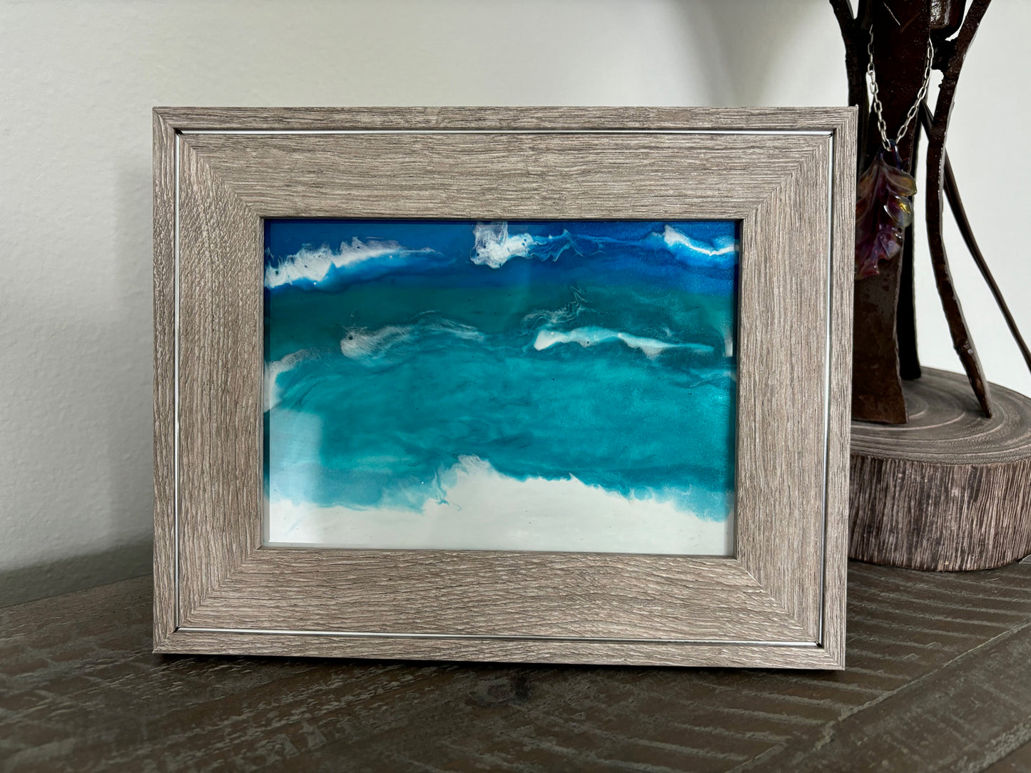 <p>I did a resin ocean scene on the glass of a photo frame. Beautiful turquoise, teal and blue water dance among the white foamy waves and white sand beach. Just like here in Panama City Beach!<Can easily hang or sit./p> <p>The resin is UV Resistant.</p> <p>The frame is a brownish/gray and has a line of silver around the whole frame.</p> <p>Overall size of the frame is about 9.5 x 7.75 inches. The glass is approximately 7 x 5 inches.</p>
