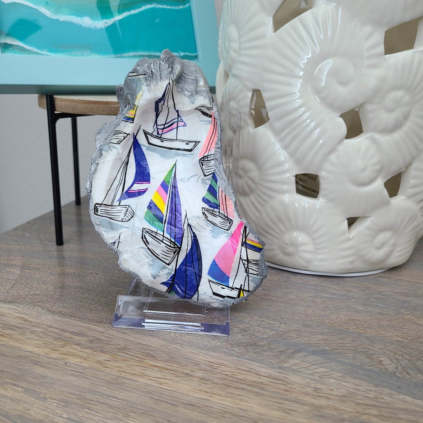 This bright and cheery oyster shell has a sailboat regatta theme. Use as a trinket dish or on the stand to accent any small area. Large Real Oyster Shell is Painted Metallic Silver on the edges and back. Finished with three coats of UV Protective spray varnish. Clear Acrylic Stand Included Approximate size: 5.5 x 3.75 inches at the widest part Accessories shown are NOT included.