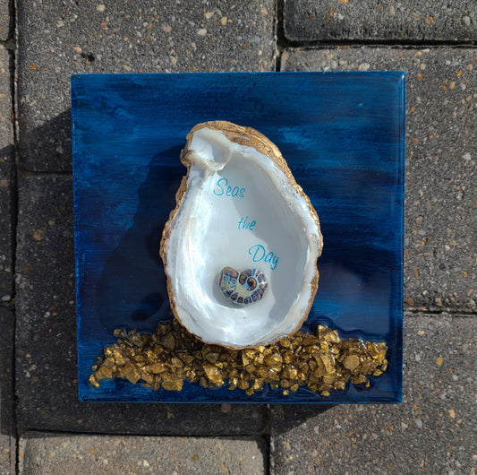 Always Seas The Day! 3-D Wall Art. Real Oyster Shell is trimmed in gold, features a small nautilus bead and gold-colored rocks. The background looks like a stormy deep sea. Unique, One-of-a-kind piece of art. The whole piece is sealed with UV Resistant Resin. Approximate size: 6 x 6 x 1.5 inches