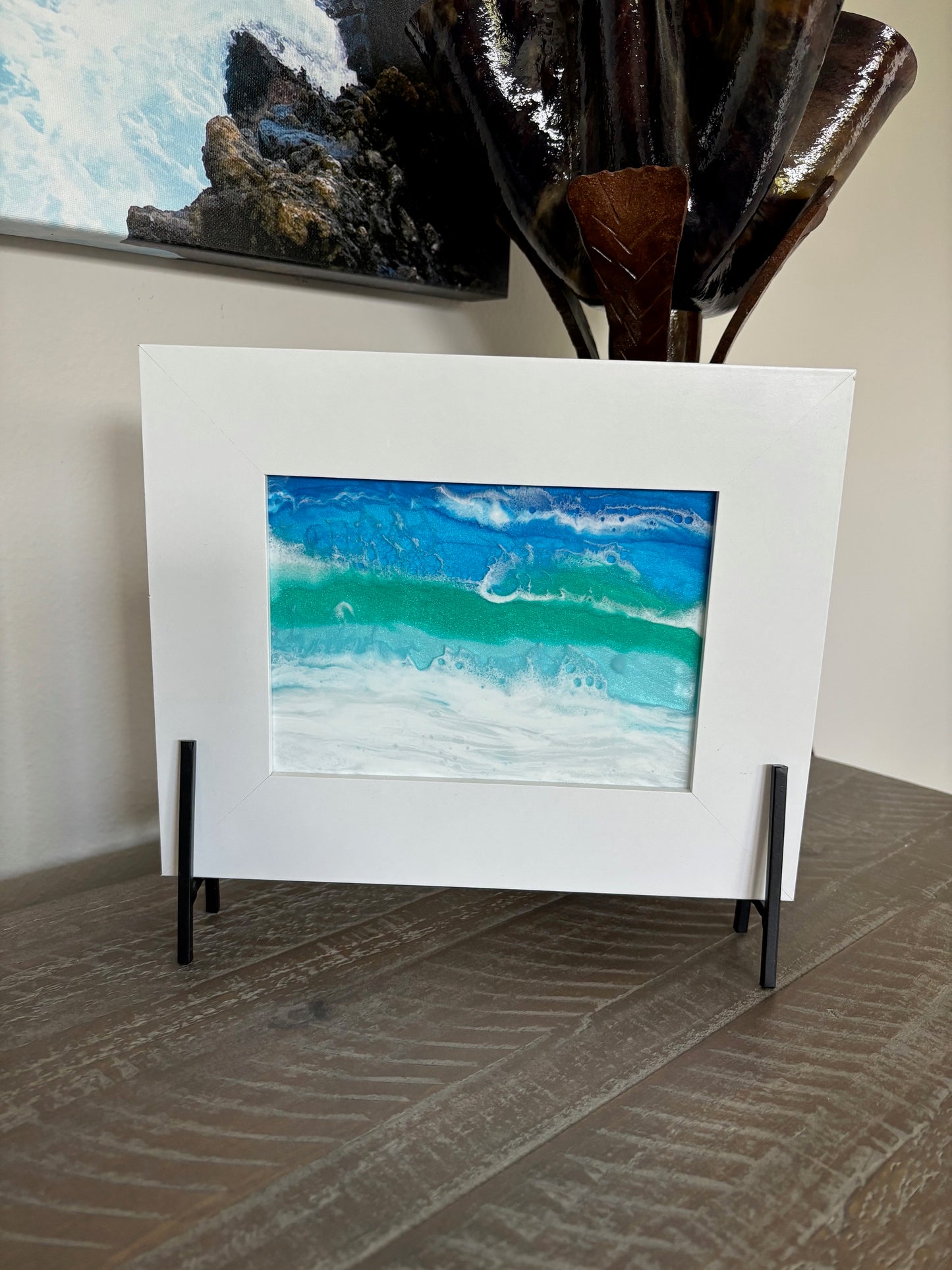 The waves in this ocean scene seem to be jumping off the glass. I love the way the waves seem 3D. I created this resin scene on glass and it sits in a white frame. The frame is attached to a black metal stand. Resin is UV Resistant. Approximate measurements: Overall: 10 x 8 inches. The glass piece itself is 5 x 7 inches.