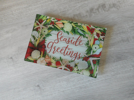 Rectangular glass serving tray has design from the underneath. Seaside Greetings. Shells, starfish, coral are intertwined with red ribbon and greenery. All looks like they are on a weathered wood background. Measures 15 x 10 inches