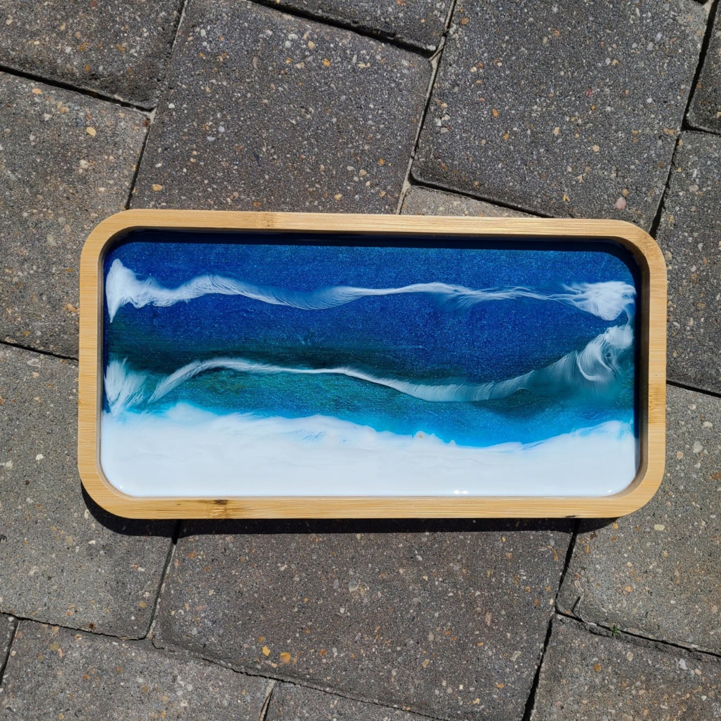 This little tray is lightweight and functional as well as beautiful. Rectangular tray with rounded corners. Deep blue and turquoise waters hit the white sandy beach. White waves play among the sparkling waters. Approximate size: 11.75 x 6.25 x .75 inches Care: Wipe with a damp cloth or an alcohol wipe.