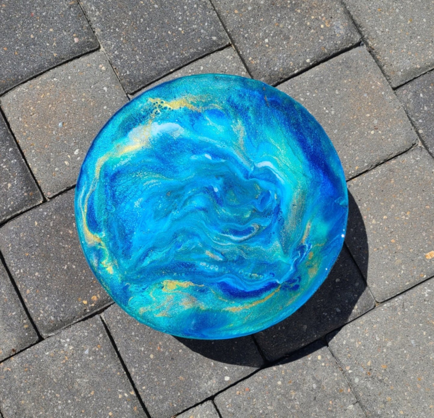 Looks like you can look deep into the water on this piece. Use as a display stand or as a trivet. Metal Legs and Heavy Wood with Resin in blues, white and gold. Resin is UV Resistant and food safe. Approximate size: 10 inches across, 3/75 inches tall overall