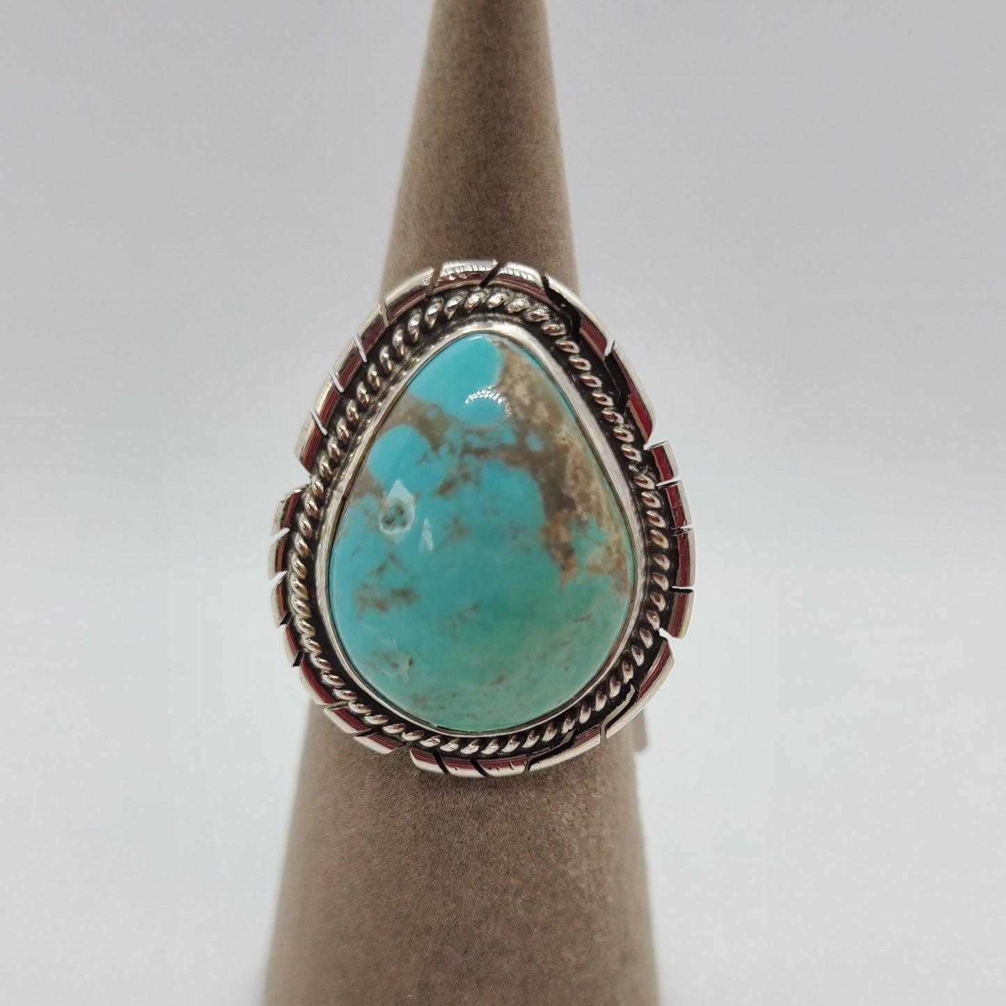 Beautiful Kingman Turquoise Ring has pear shaped stone. Light greens gently fade into light blue with brown matrix. Bezel set in Sterling Silver with twisted rope. Backplate has saw cuts. Split Band Navajo Artist, Dave Skeets Size 8 Stamped: Sterling, Skeets (the band is over part of his name) Certificate of Authenticity guarantees Native American Made