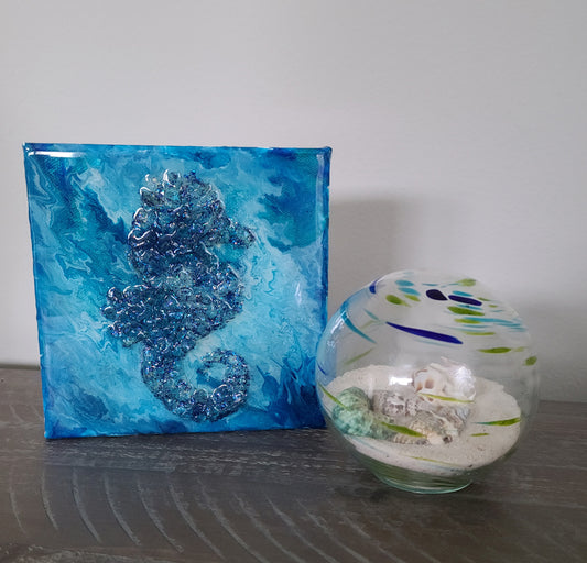 Mixed media art. 6 x 6 Canvas. Seahorse made of crushed glass with a multi blue color background. Looks like he's floating underwater. The entire piece is coated in resin that is UV resistant. One inch wide canvas allows this piece to sit on a table or shelf or it can hang.
