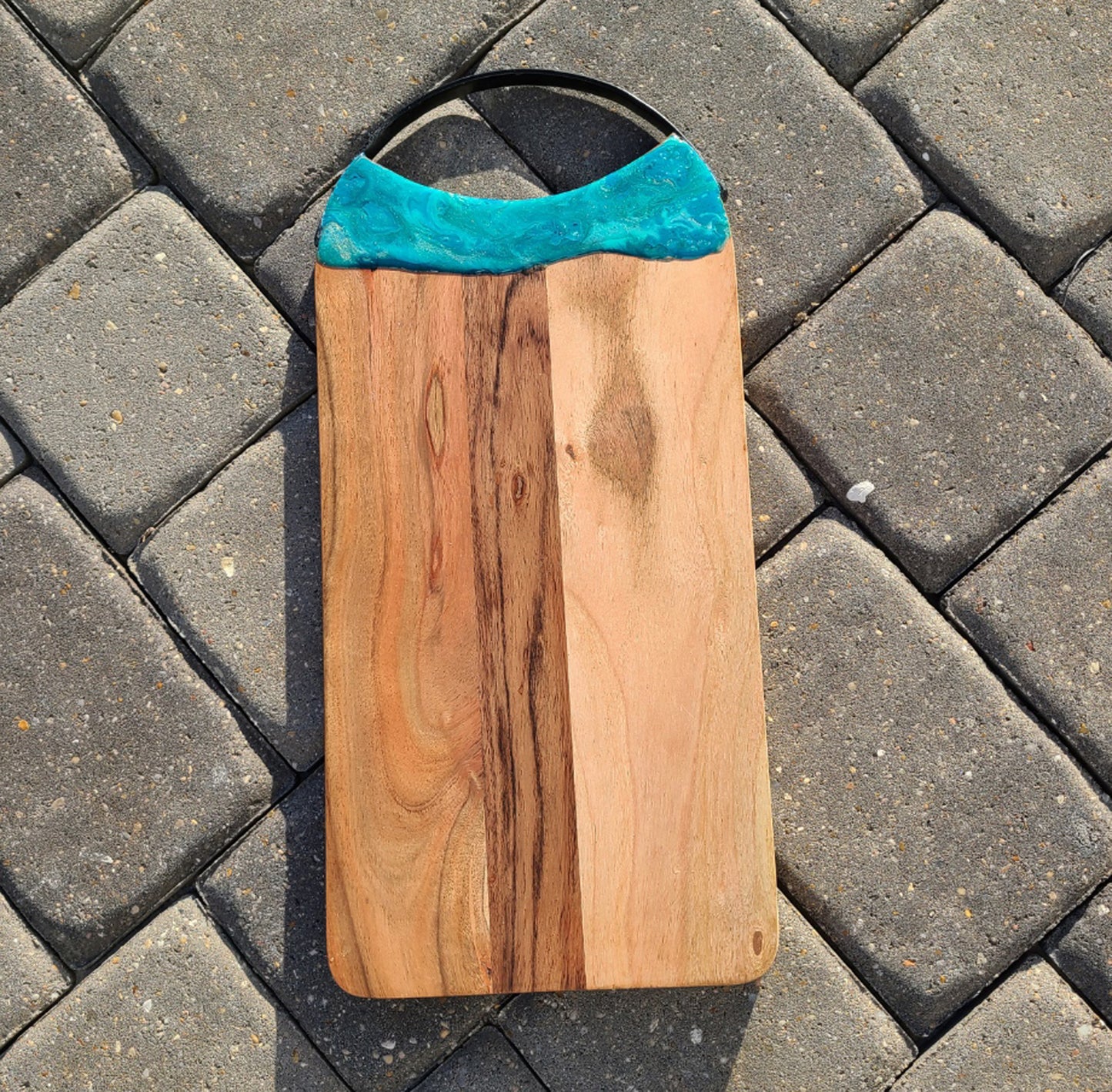 Cutting Board with curved metal handle at the top. Metal handle is black. Resin accent on top end in teals, green and gold. Really sparkles in the light. UV and food safe resin. Overall length is 17 inches including the handle. 8 inches wide.