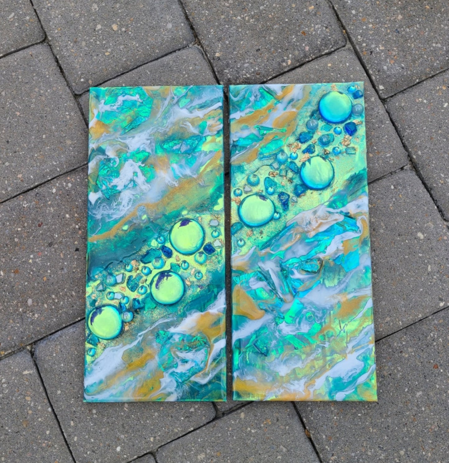 I had so much fun creating this mixed media piece! Created on wood panels. Glass pieces, holographic paper, resin and glitter. So much texture in this piece. Colors of teal, gold and white, but the holographic paper makes it glow different colors as well. Cork backing and saw tooth hangers. Each piece measures 5.25 x 12. Overall dimensions when hung approximately 10.5 x 12 depending on how close you hang them together.