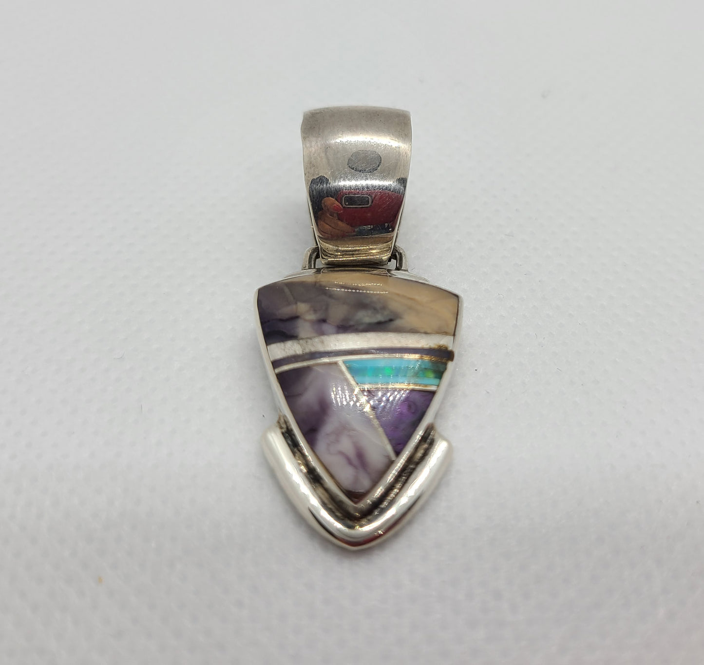 Mostly purple pendant. Sections of Charoite, sugilite and opal, separated by small pieces of silver. Triangle or arrowhead shape. Large silver bail. Stamped on the back, Francisco A., Sterling.