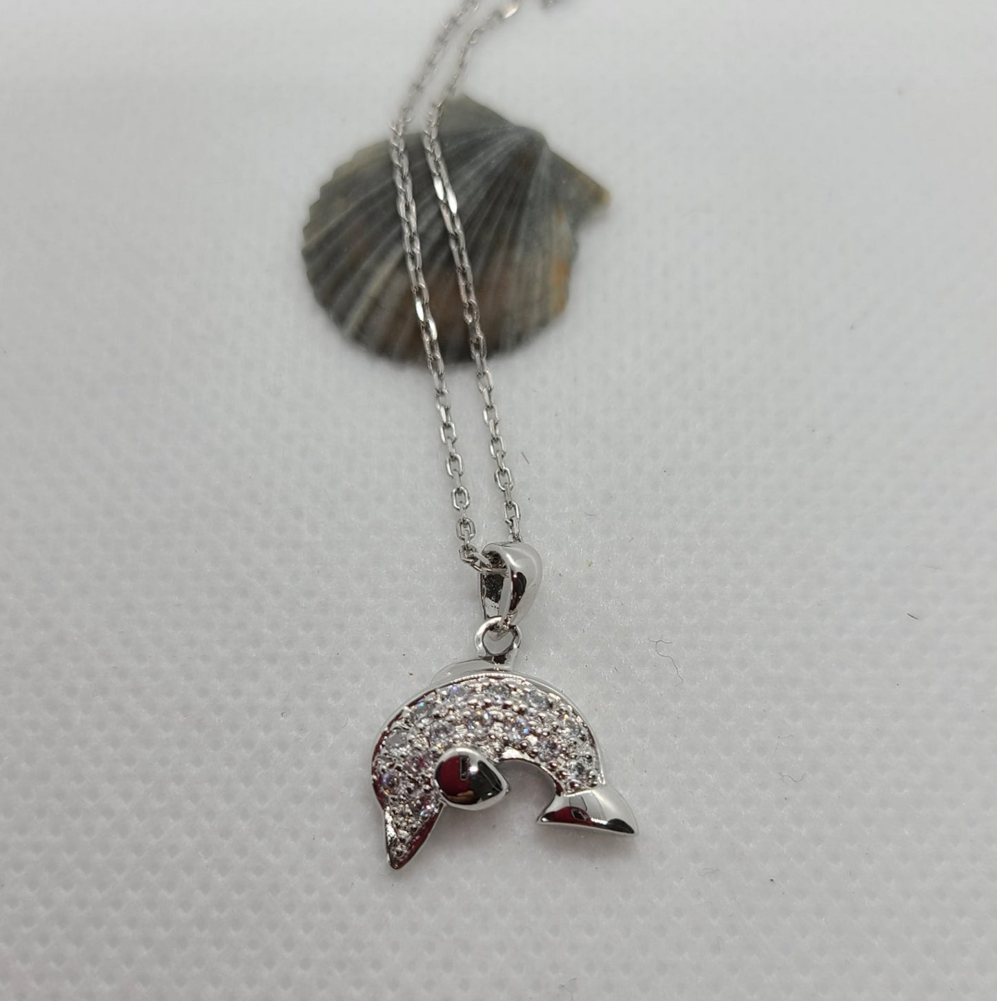 Curved silver dolphin. Body is covered in CZ's. Nisha Design Jumping Dolphin Necklace. Sterling Silver and CZs. Rhodium Plated. Beautiful design. Chain is Sterling Silver and is Rhodium Plated. Never needs polishing. Chain is 16 inches long.