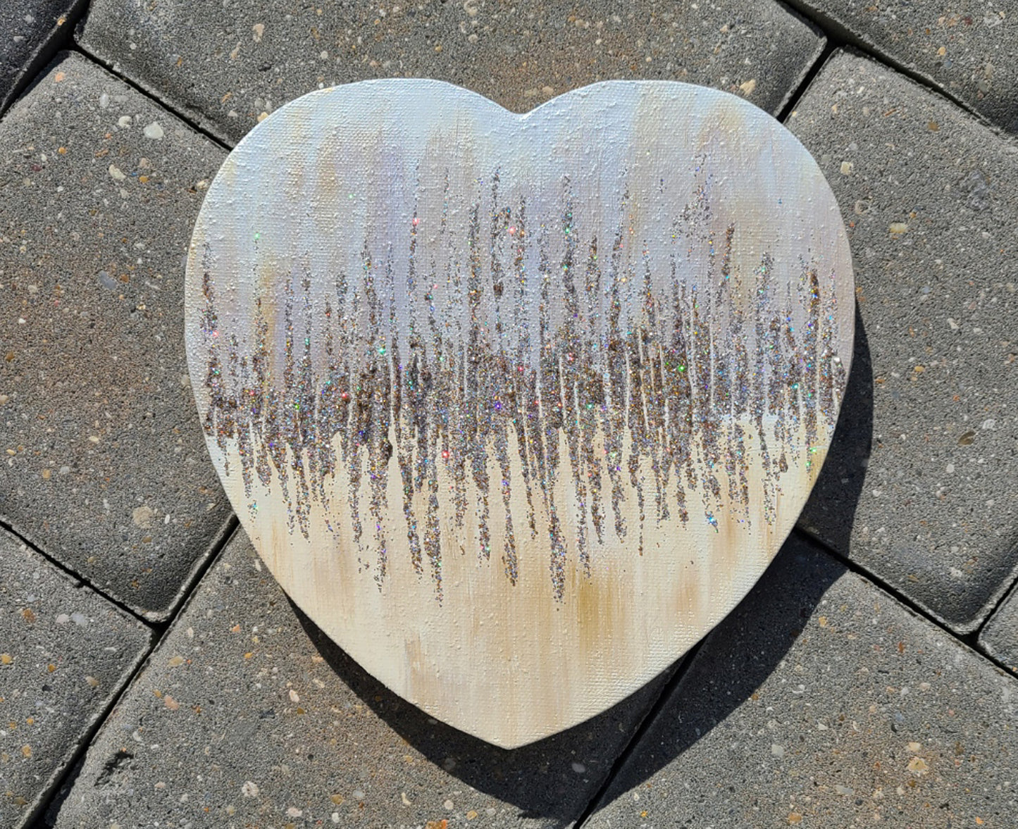 8 inch tall heart shaped canvas. Painted in a Shabby Chic style, off white with shades of gold and brown overlay. Center line of various metal tones of glitter are spread up and down for an effect that looks like a fast heartbeat.