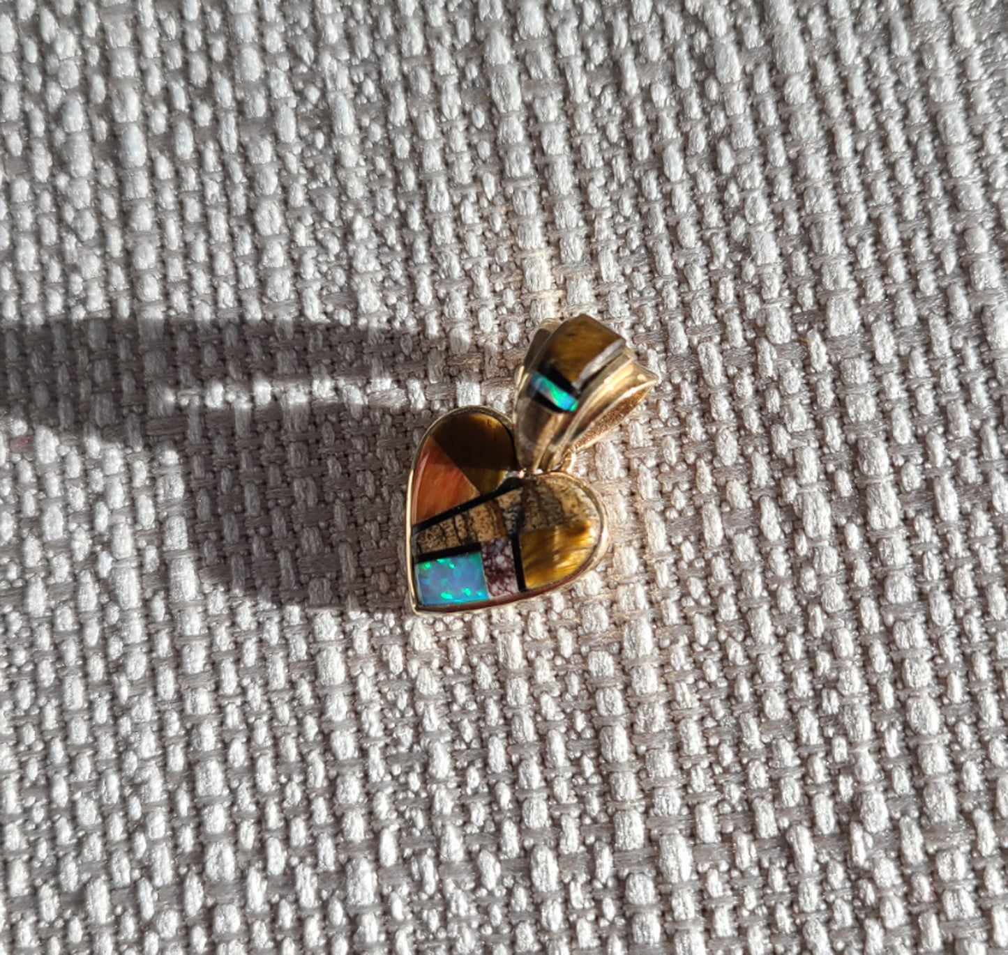 Native American Inlay heart pendant is set in 14kt gold. Tiger's eye, opal, picture jasper, spiny oyster, and thin lines of onyx between the stones. Bail is decorated with same stones. Reverse side has a dwelling scene. Approximate size 1 inch.