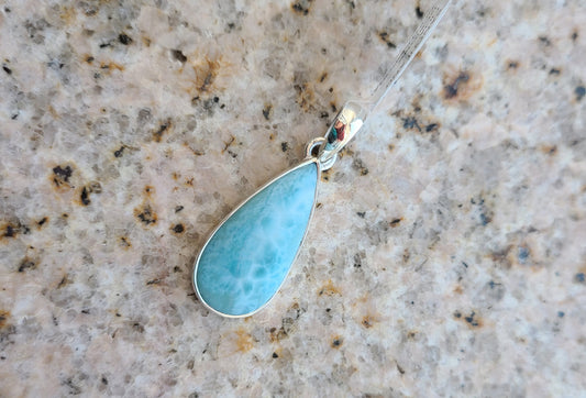 Larimar is only found in the Dominican Republic and is often called the Blue Jewel of the Caribbean.  This is a teardrop shaped stone. Bright ocean blue with splotches of darker blue and white webbing. Set in a simple contemporary setting of a silver bezel and bail. Overall length is approximately 1.25 inches.