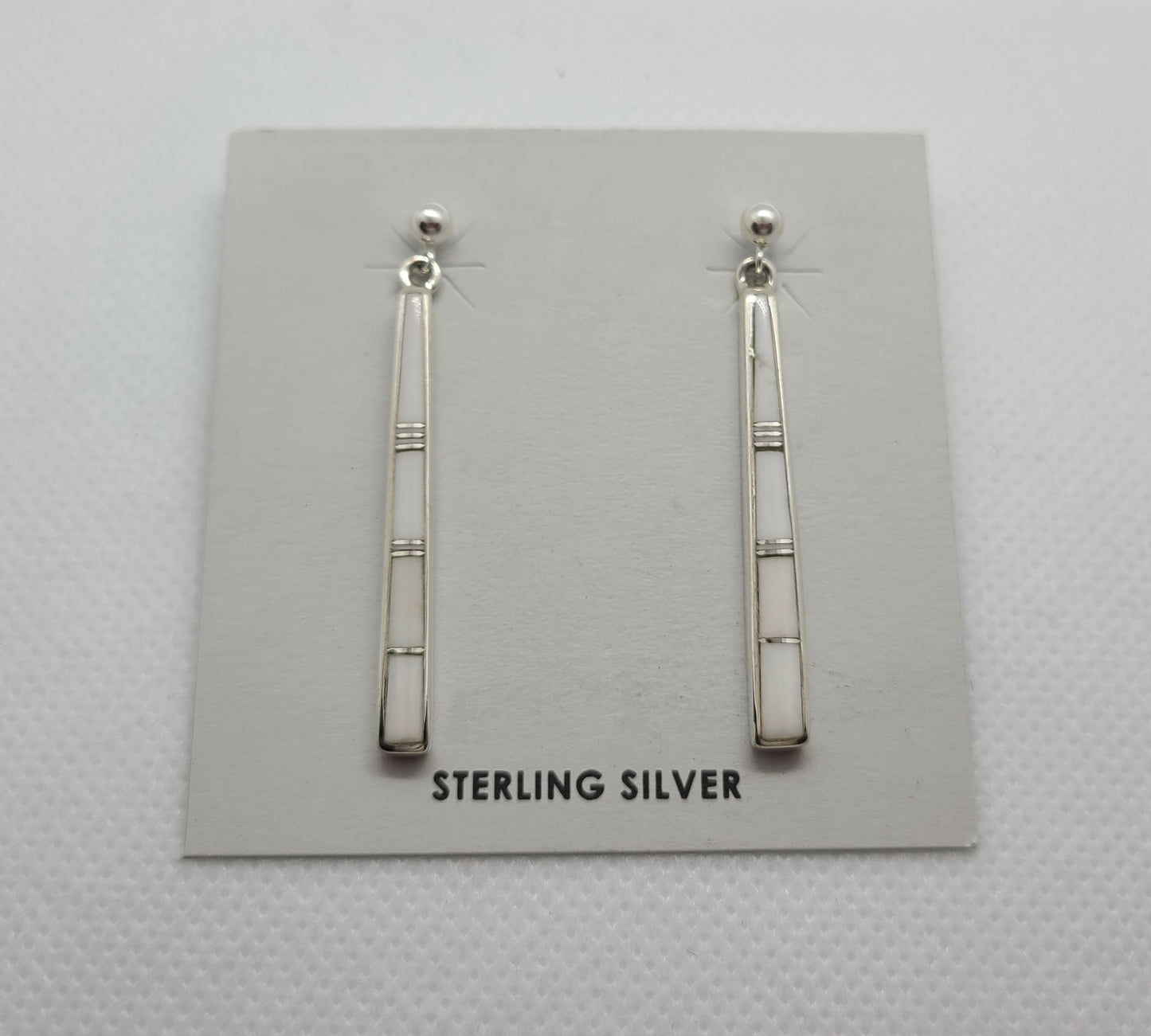 These earrings are stick like, White Buffalo stone inlaid in Sterling Silver with small slivers of silver between the stones. Mostly pure white with a very small amount of matrix. Approximately 1.5 inches long. Navajo artist Rick Tolino. Comes with Certificate of Authenticity.