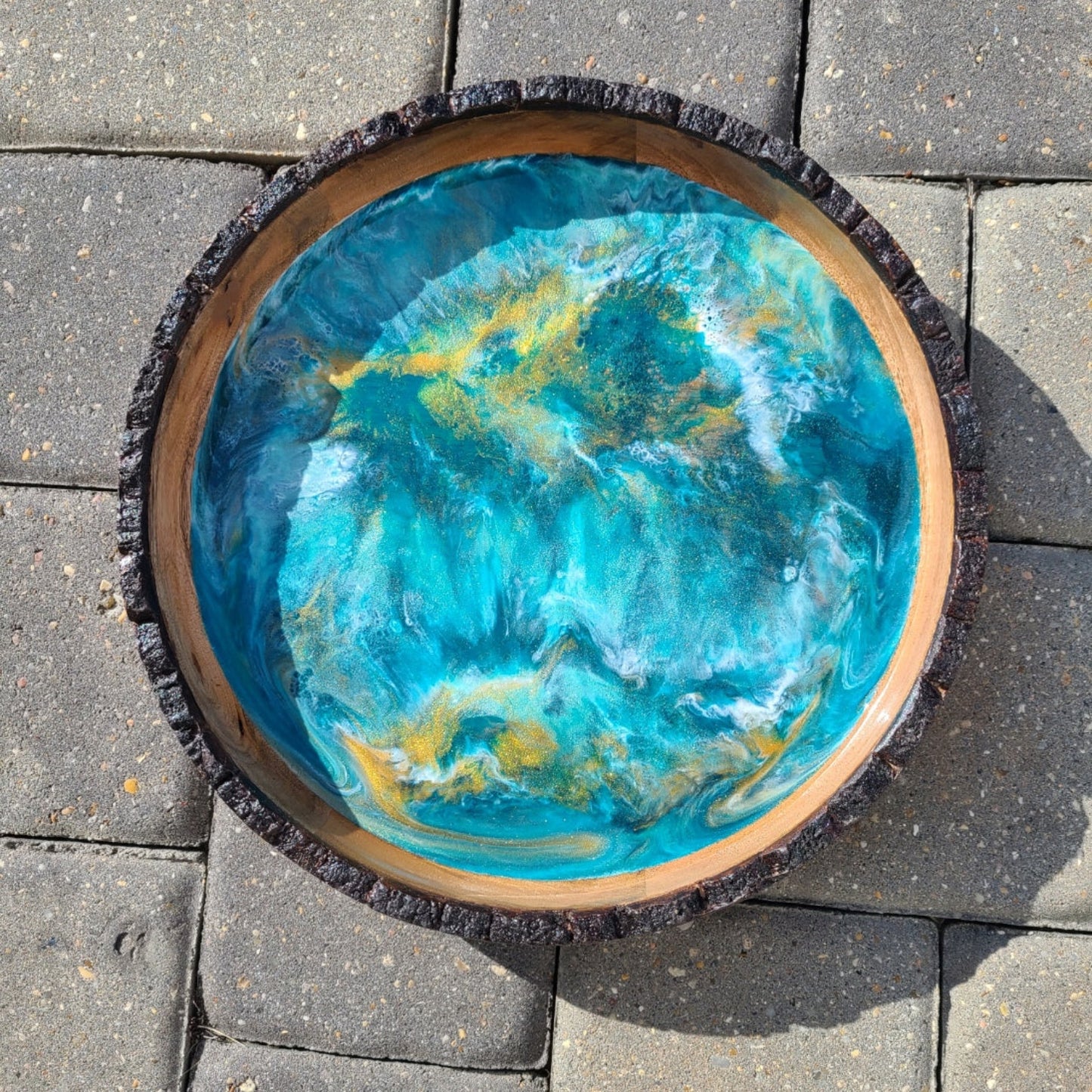 Turquoise and teal swirl around the gold and white in this round wood tray. The Gold sparkles and seems to hover over the other colors. Resin is UV Resistant and Food Safe Useful as well as beautiful. Approximate size: 11.75 inches round; 1.75 inches deep