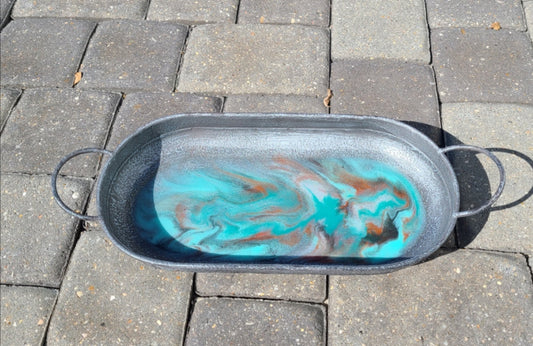 This tray turned out beautiful. The colors are dark pewter, burnt umber, Seafoam green, teal green and pearl. A second layer of resin adds depth. There is a lot of sparkle throughout. Oval metal tray Resin is UV resistant and food safe Round ball feet on bottom Approximate size: Handle to handle 18 inches; 7.5 inches wide; 2.5 inches tall Wipe with a damp cloth and hand dry. Resin can also be cleaned with an alcohol wipe.