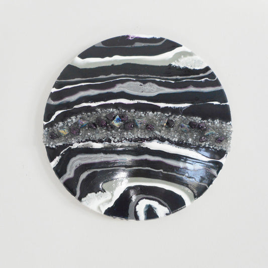 18 inch round wood has bands of deep purple, metallic silver, gray, and metallic white. A large band of crushed glass, rocks, chunks of rainbow titanium and crystals flow through the middle. Two smaller areas of crushed glass in opposite corners. A very striking statement piece.