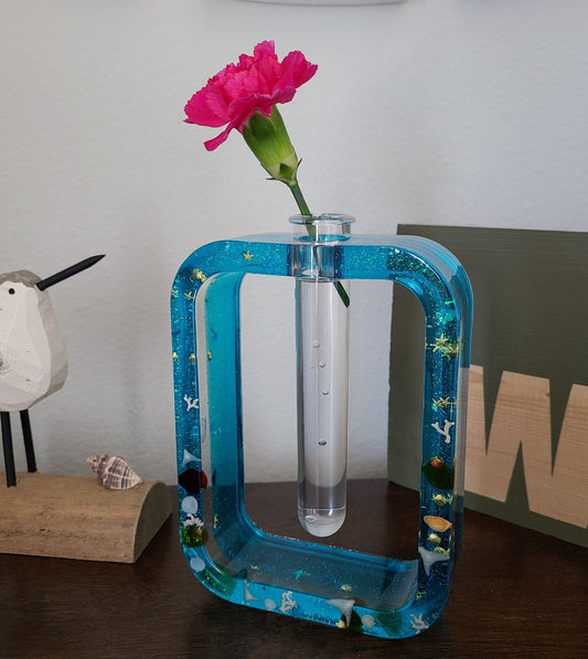 Useful as well as beautiful. I created this rectangular vase at my home in Florida. The shells and "mermaid's tails" came from local beaches. Embellished with gold leaf and accents. Can be used to display a small arrangement, bud vase or for propagation of new plants. You can see the plant's progress while it grows. Made of durable resin Plastic tube included (but the flower is not) Approximate size: 5.5 inches tall; 4 1/8 inches wide and 1.5 inches deep