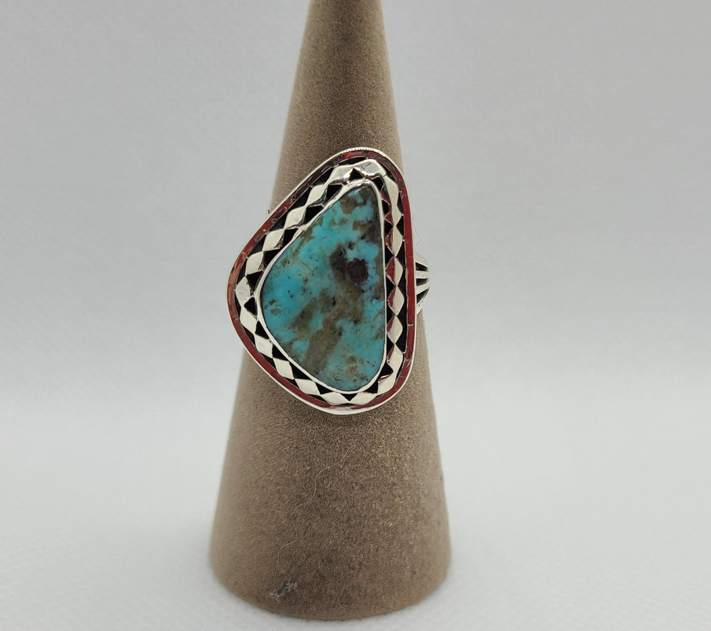 Kingman Turquoise ring has an asymmetrical triangle stone with soft rounded edges. The stone is a medium blue with brown and black matrix. The bezel has a continuous diamond design around the stone resting on the backplate. Split band design. Unisex. Size 9