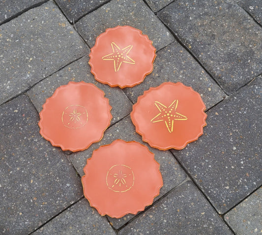 Sunset orange coasters with gold sand dollars and starfish. Created with UV Resistant and Food Safe Resin Designs won't rub off because they are protected with resin Gold painted trim on the sides The close up photos have a reflection on them that looks like spots, but that is only a reflection Approximate size: 4.75 x 4 inches