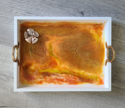 This little tray is lightweight and versatile. Can't you feel the sun shining on your face? One of a Kind piece. Sunrise or Sunset? Remember that Summer vacation? You will when you look at this. Swirls of yellow, orange and gold dance together. A cluster of shells in the corner give dimension to the tray. White tray is wood (MDF) with brushed gold round handles. Resin is UV Resistant and Food Safe. Approximate measurements: 11.5 x 9 inches