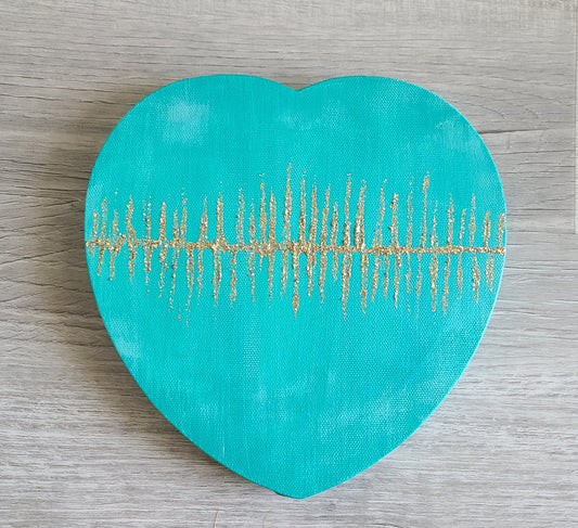Shades of teal and metallic blue green on heart shaped canvas wall hanging. The middle across side to side has lines of glittery gold and silver. Approximately 8 inches.