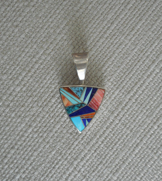 Triangle shaped pendant is made of turquoise , lapis, and spiny oyster stones with tiny pieces of silver between the pieces of stone. All set in Sterling Silver. The reverse side has an intricate overlay design. A large bail that spins. Overall length is 1.5 inches.