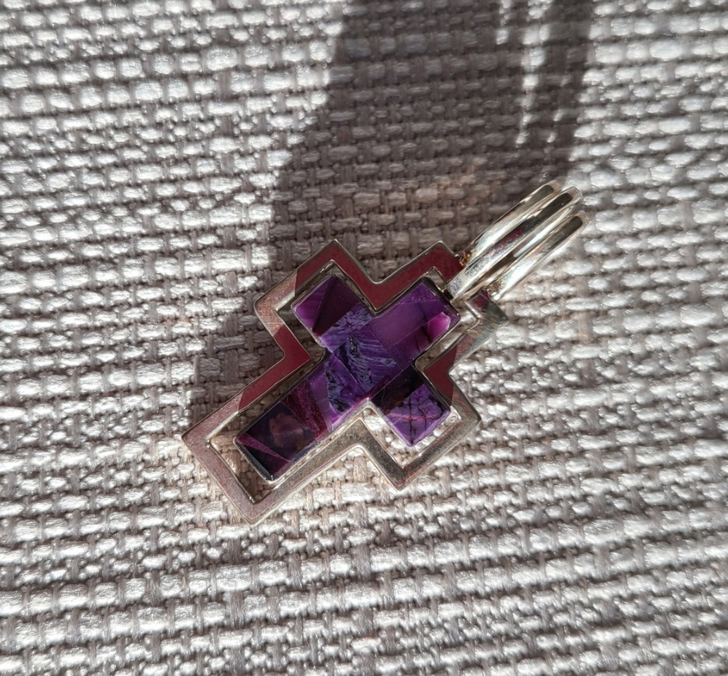 Cross Pendant made of Sterling Silver and Sugilite. Called the Trinity because it can be worn 3 ways. The sugilite cross by itself, the Sterling cross or together where the sugilite cross fits inside the silver cross. Overall length is 1.75 inches. Made by Gertrude Zachary.