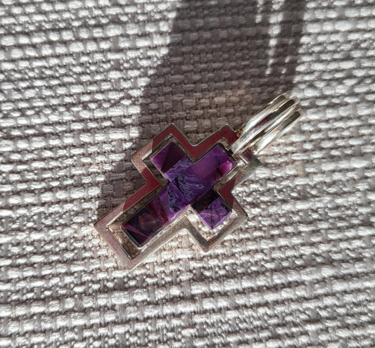 Cross Pendant made of Sterling Silver and Sugilite.  Called the Trinity because it can be worn 3 ways. The sugilite cross by itself, the Sterling cross or together where the sugilite cross fits inside the silver cross. Overall length is 1.75 inches. Made by Gertrude Zachary.