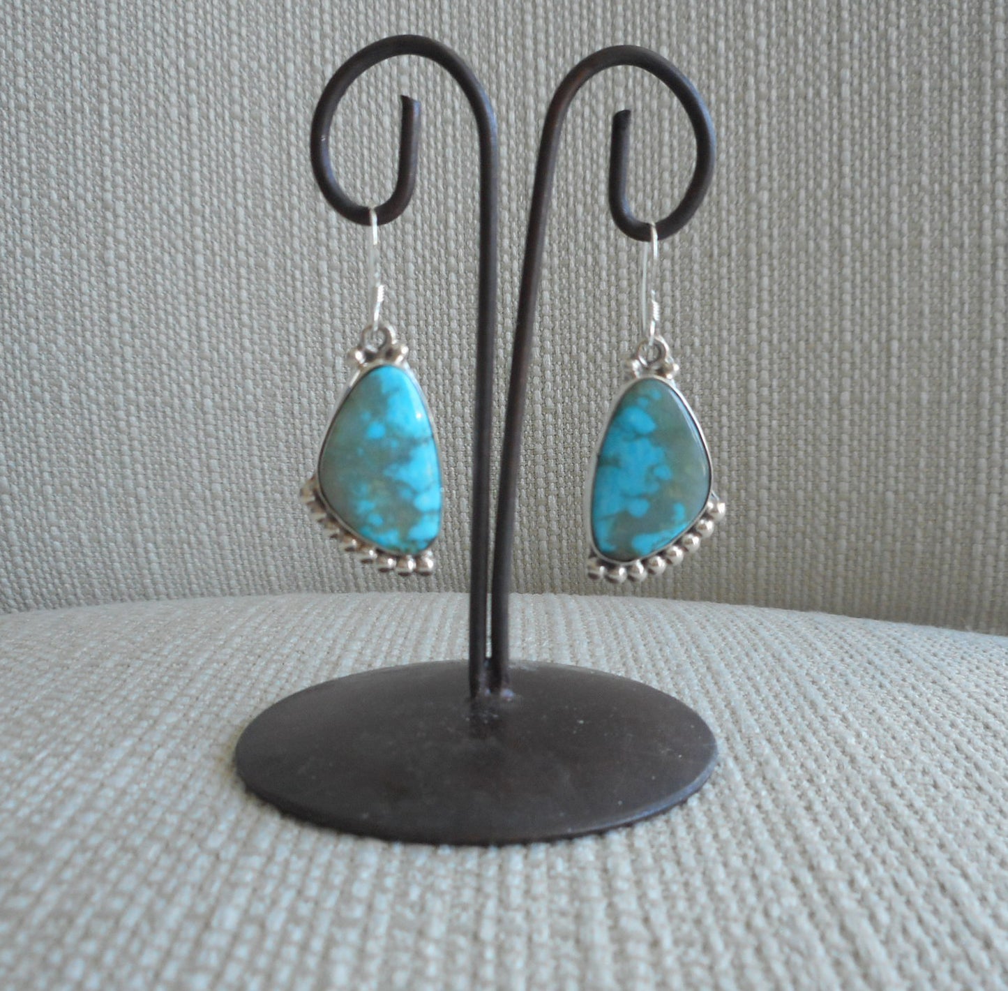 Kingman Turquoise dangle earrings. Beautiful shades of blue in the stunning earrings. Set in Sterling Silver with beads of silver accent on the top and bottom of these freeform stone earrings. Artist Sharon McCarthy. Approximately 1.5 inches long. Native American. Comes with Certificate of Authenticity.