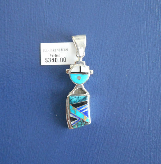 Round faced Yei pendant is made of inlaid stones of turquoise, only, lapis and Mother of Pearl.  Cut out silver around the head and on the neck. Silver bail.  2 inches long including the bail and .50 inches wide.