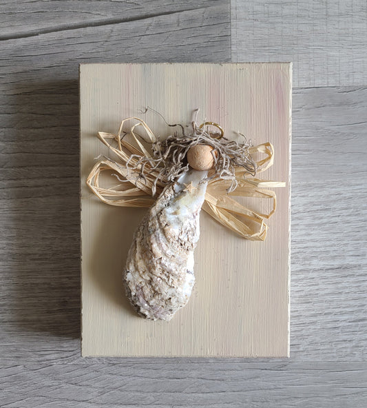 This sweet little angel has lots of personality. Her body is made of an oyster shell that has been coated with acrylic spray and varnish and then sprinkled with chunky glitter. She is on a distressed wood base for hanging on the wall. She's too front heavy to stand on a shelf unless you place something a little heavy on the inside of the frame. Approximate size: 7 x 5 x 1.5 inches