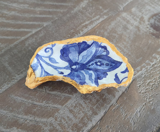 Beautiful, handcrafted oyster shell can be used alone or as a trinket holder.  Blue flower on white background. Trimmed in gold paint.  Coated with 2 coats of Varnish. The back has a coat also to protect it from flaking and leaving dust behind.  Note: Rings NOT included  Approximate size: 3.75 inches at the longest point, 2 inches wide at the widest point.