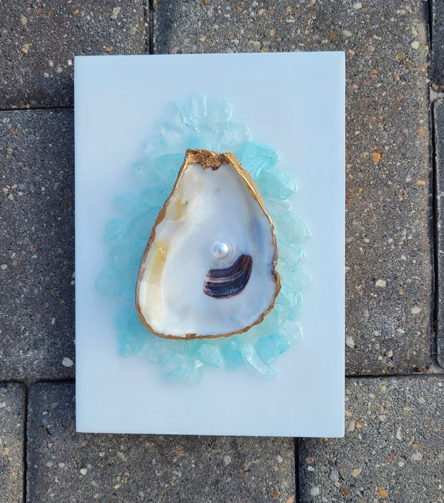 Original little piece of art.  Accent a bathroom, shelf or most anywhere a small piece of art will liven up your room.  A real oyster shell holds a pearl.  I trimmed the shell in gold and placed it on a wood canvas.  The shell lays nestled on blue crushed glass on a white board.  The piece is covered in resin so that it looks like it is laying in water.  5 x 7 x .75 inches  If you would like it signed on the back, leave a message.