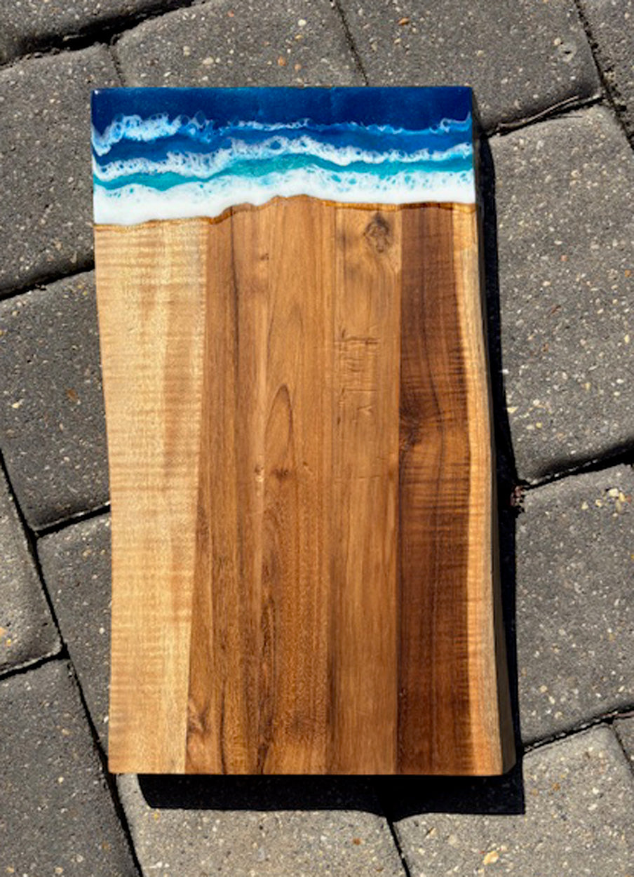 Beautiful, heavy board makes the perfect gift. Practical and beautiful too! The foamy ocean goes from deep, dark blue to light turquoise water with dancing white water. Resin is UV Resistant and Food Safe! The edges of the wood are wavy.  I believe the wood is Acacia. Approximate size: 15 x 8.5 x 1 inches Care: Occasionally treat the wood with Food Grade Mineral Oil or Olive Oil.  Wipe the resin with a clean damp cloth or an alcohol wipe.