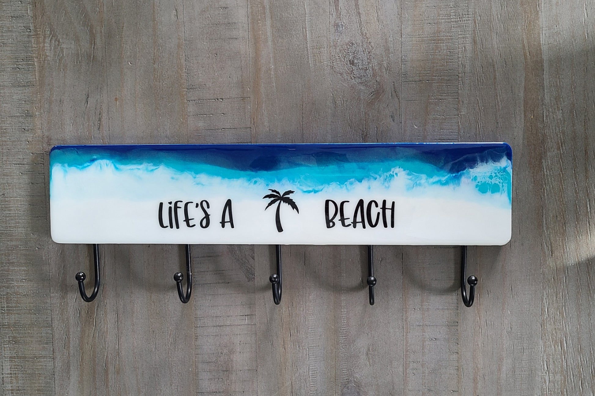 I used resin to create this beach and water scene, lots of sparkle if you look closely.  White waves crash over the colorful water.  LIfe's A Beach With Palm Tree.  A clear coat of resin was poured over the words so that they will not peel off.  Lightweight wood  Resin is UV resistant.  Metal hooks for hanging towels, kid's clothes, leashes or hats.  Approximate size: Wood: 18 x 4 inches; hooks add another 2.5 inches.  Key Holes on back for hanging.