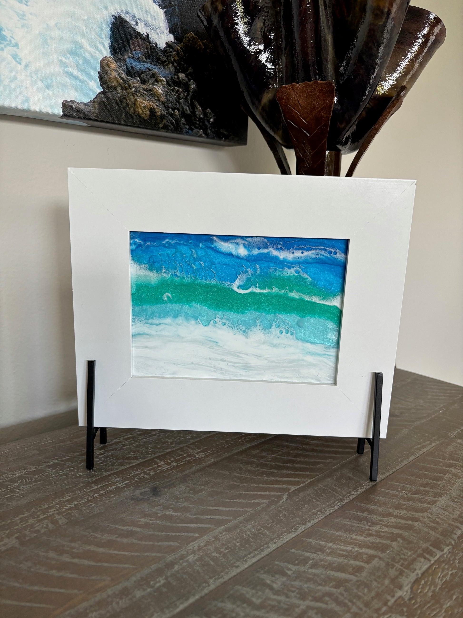 The waves in this ocean scene seem to be jumping off the glass. I love the way the waves seem 3D.  I created this resin scene on glass and it sits in a white frame. The frame is attached to a black metal stand.  Resin is UV Resistant.  Approximate measurements: Overall: 10 x 8 inches. The glass piece itself is 5 x 7 inches.