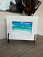 The waves in this ocean scene seem to be jumping off the glass. I love the way the waves seem 3D.  I created this resin scene on glass and it sits in a white frame. The frame is attached to a black metal stand.  Resin is UV Resistant.  Approximate measurements: Overall: 10 x 8 inches. The glass piece itself is 5 x 7 inches.
