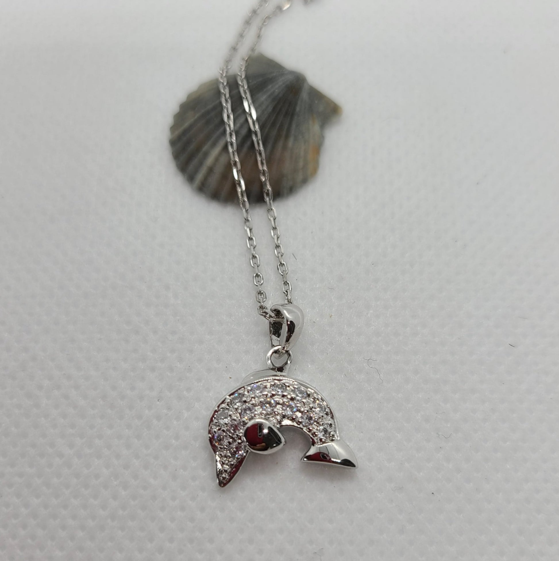 Curved silver dolphin. Body is covered in CZ's. Nisha Design  Jumping Dolphin Necklace.  Sterling Silver and CZs. Rhodium Plated. Beautiful design.  Chain is Sterling Silver and is Rhodium Plated. Never needs polishing.  Chain is 16 inches long.