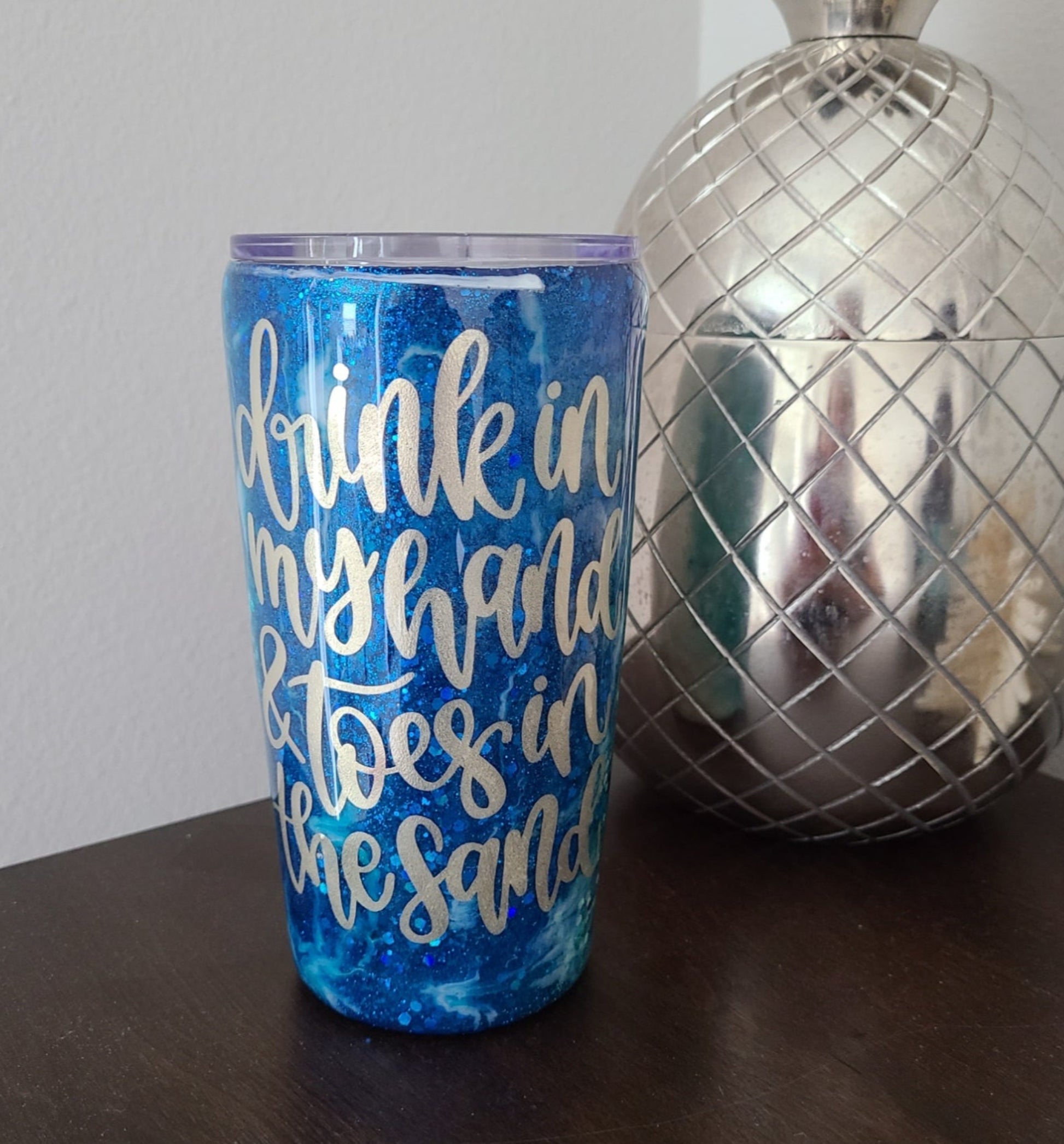 Tumblers are a challenge to make, especially on a vertical design.  But I love how this one turned out.    Drink in my hand & toes in the sand. Two layers of resin over the decal ensure that it will not come off.  Various colors of the ocean sparkle through as the white waves of the ocean breaks onto the sand.   20 oz.  Double Wall Stainless Steel under the resin.  Comes with lid, straw and cleaner.  Hand Wash only in warm water.  DO NOT put in the dishwasher.