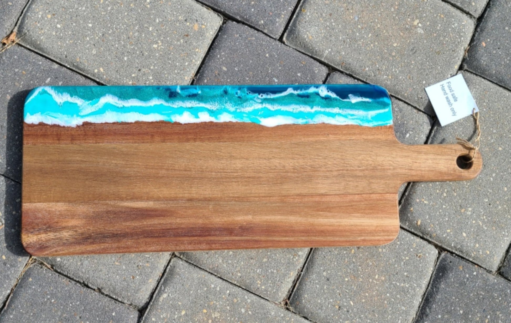 I recently created this cutting board with resin to look like the ocean. I call it "Foamy Ocean" because the water looks like it has lots of foam. Acacia Wood Great gift or reminder of the ocean. Would make a beautiful charcuterie board. Food safe wood and resin Care: Wipe with a damp cloth or resin can be clean with an alcohol wipe.  Occasionally, treat the wood with Food Safe Mineral Spirits or Olive Oil. Approximate size: 20.5 inches long; 7.5 inches wide; .5 inches thick