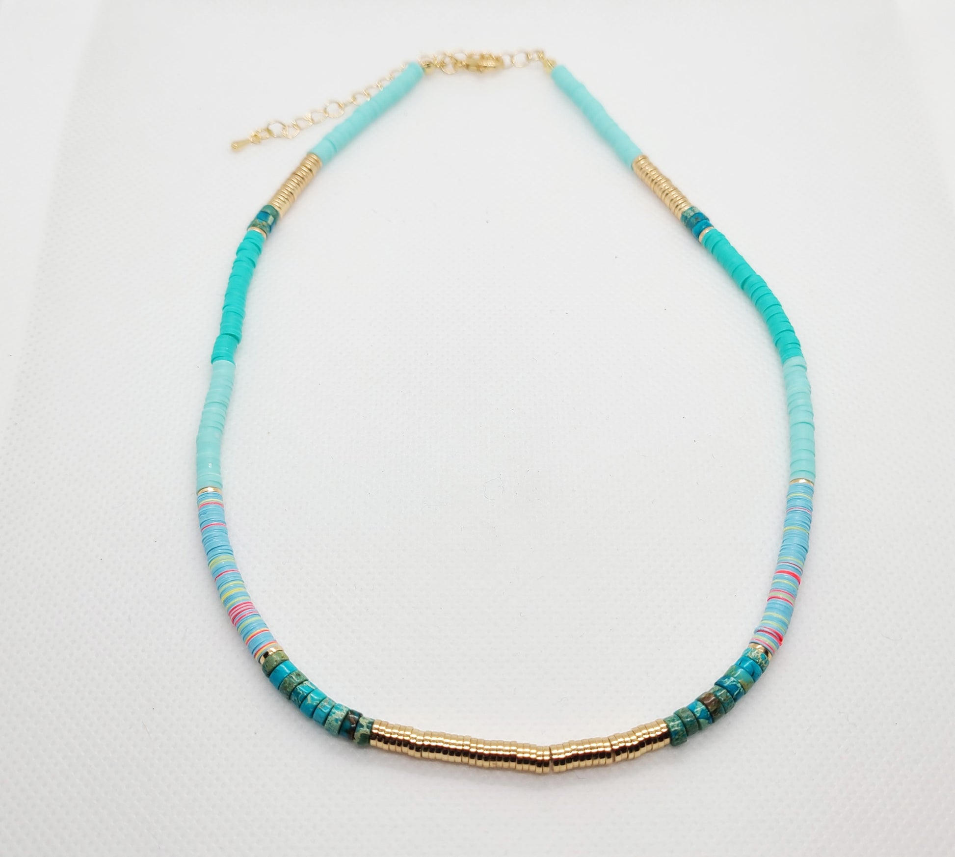 Adjustable Length necklace.  Disc like beads called Heishi make up this bright beautiful necklace.  Various shades of turquoise accented by a few pink beads and gold tone metal beads along the front few inches and other sections of gold in various parts of the necklace. Necklace is 16 inches with an additional 3 inch extender.