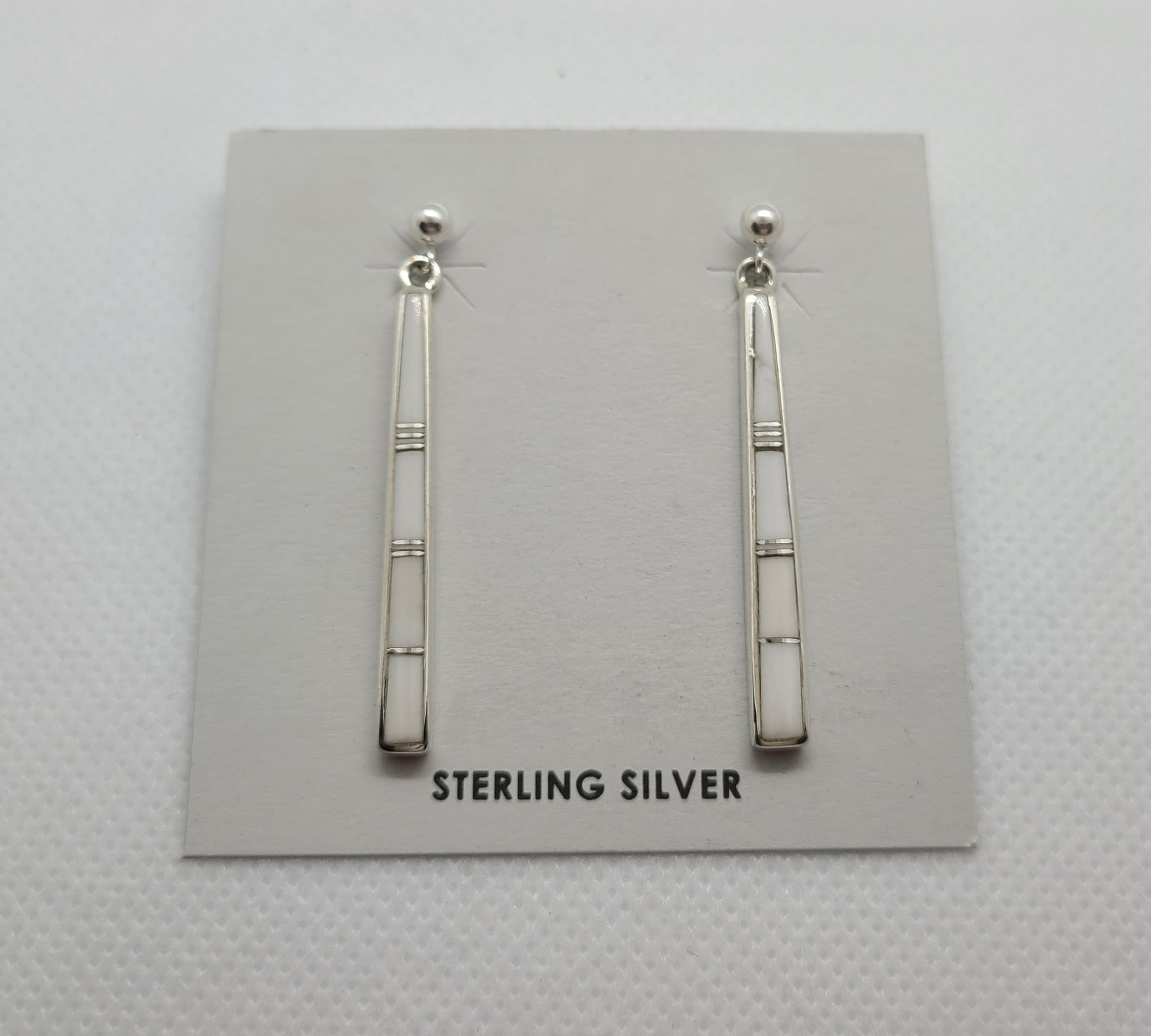 These earrings are stick like, White Buffalo stone inlaid in Sterling Silver with small slivers of silver between the stones.  Mostly pure white with a very small amount of matrix. Approximately 1.5 inches long. Navajo artist Rick Tolino. Comes with Certificate of Authenticity.