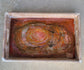 Love the design on this distressed wood tray. Oranges, Pinks, Gold and Pearl and Brown resin show off the style of this tray. There are a few bubbles in the resin that I tried to capture on the pictures, but they don't distract from the beauty of this piece. Cut out handles. Metal corner accents. Light wood with white distressed look Approximate size: 18 x 11.5 x 2.75 inches Resin is UV Resistant and Food Safe. Use a damp cloth or an alcohol wipe to clean the resin.