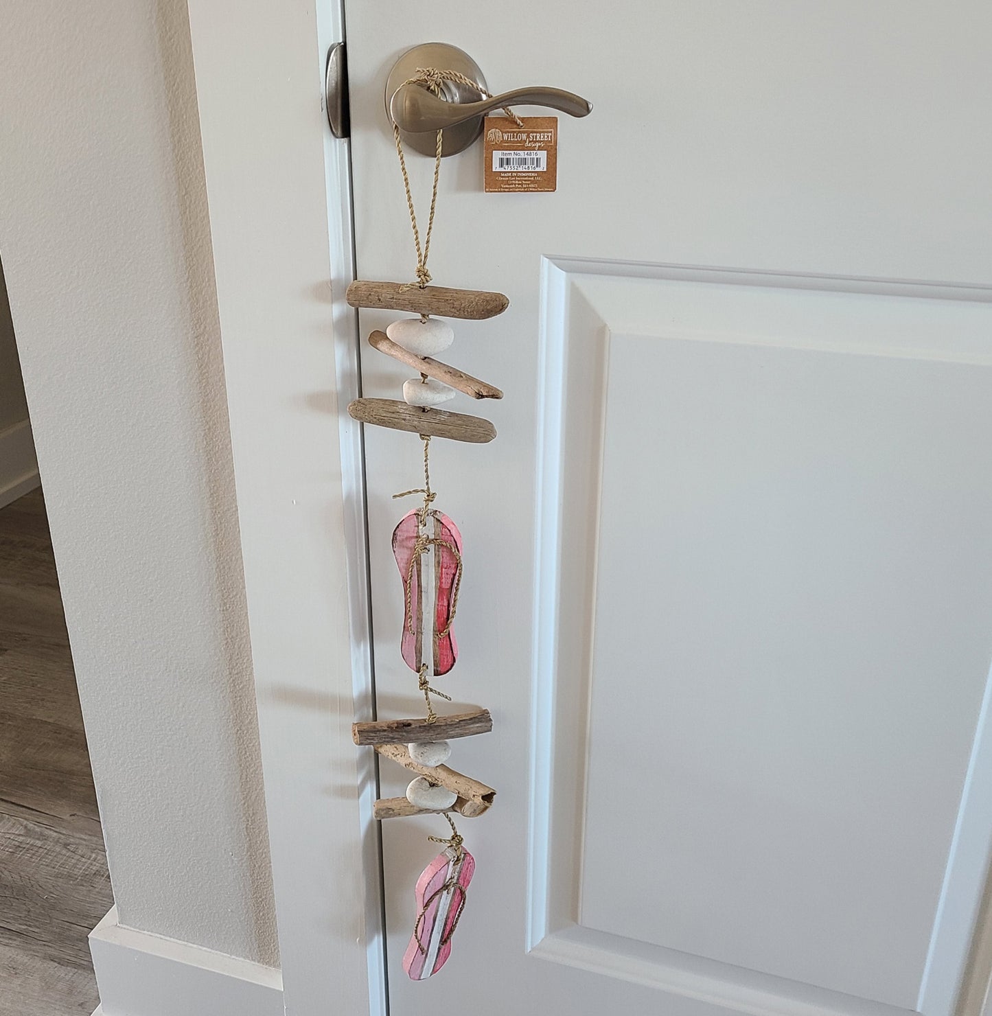 Two wood cut out flip flops are pink with white stripes.  Six pieces of round wood are separated by white stones.  All are hung on a jute rope and the top has a big loop for hanging.  Great for indoors or out.  Overall length is approximately 27 inches.