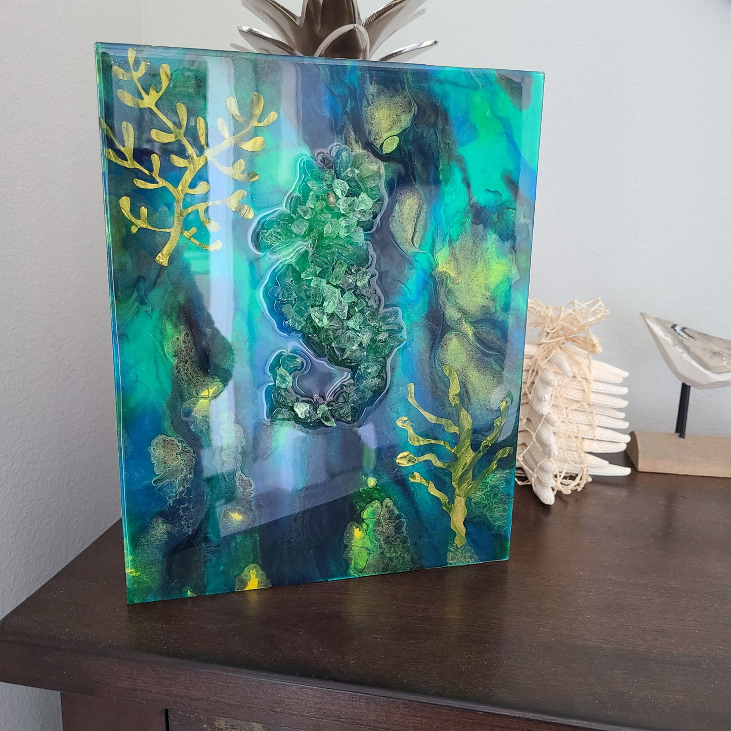 Adorable little seahorse floats in his underwater habitat.  I love the beautiful background of blues, gold and green.  The seahorse floats among seaweed.   Crushed glass and resin on wood.  This piece can stand or hang.  Approximate size: 8 x 10 x 1 inch  Note: the first photo has a glare, there is no white in this piece.